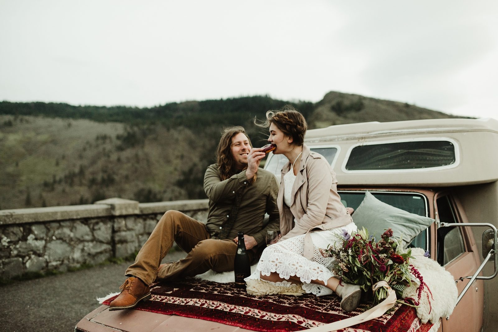 Couple sitting on hood of their camper eating donuts to celebrate their elopement