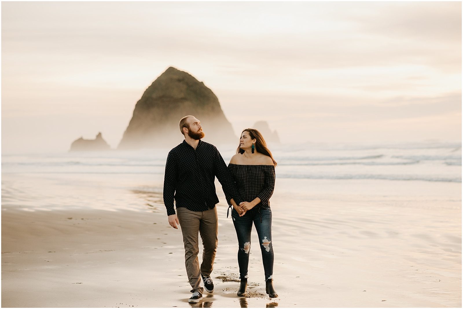 Couple walking on the sand at sunset at Cannon beach with Haystack rock in the background