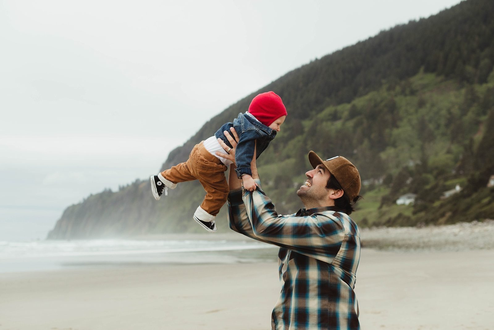 Young dad throwing infant son into the air during family session at Manzanita Beach, Oregon