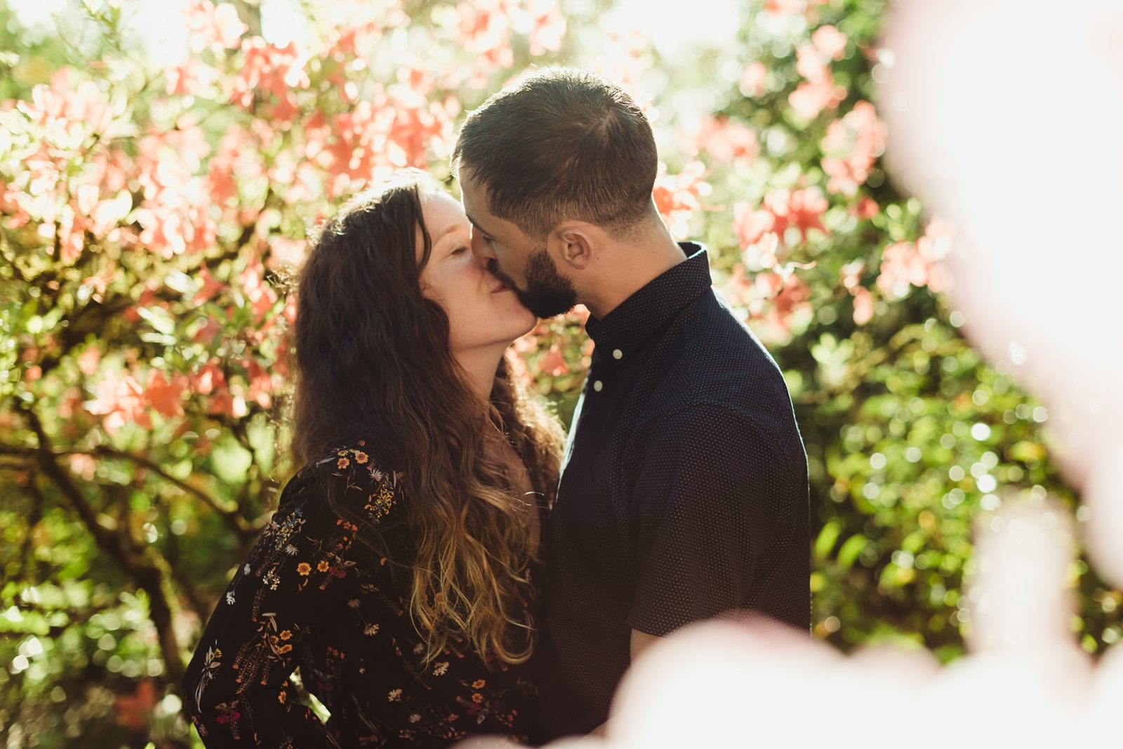 Couple kissing among flowers during engagement session at Crystal Springs Rhododendron Garden 