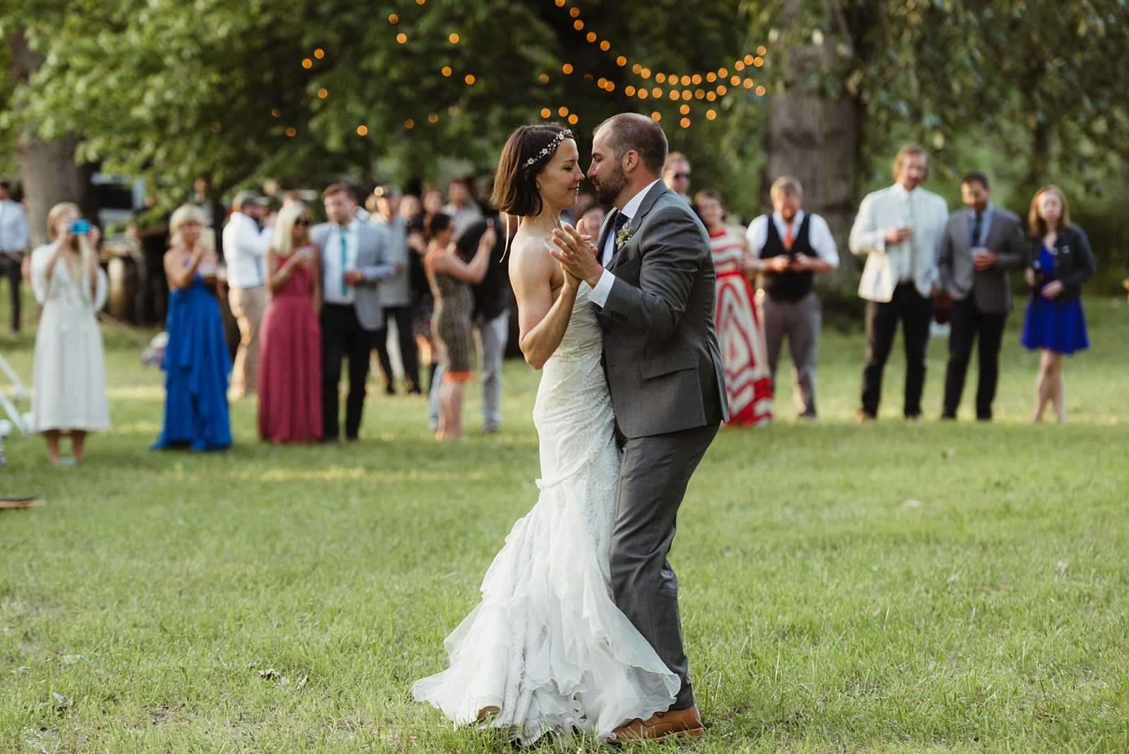 First dance in the grass under cafe lights at a summer wedding