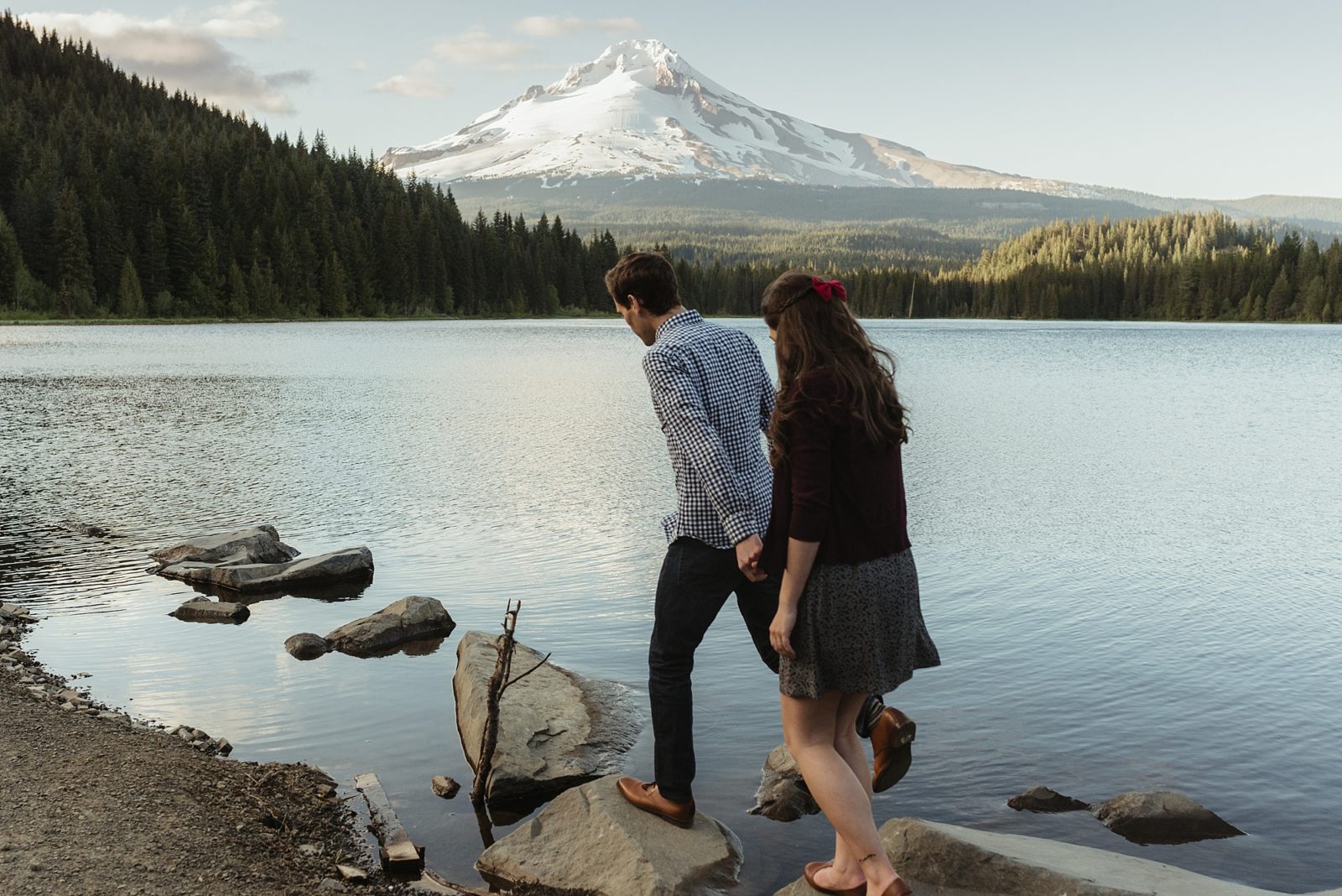 Couple walking on rocks in Trillium lake with Mt. Hood in the background during their engagement session