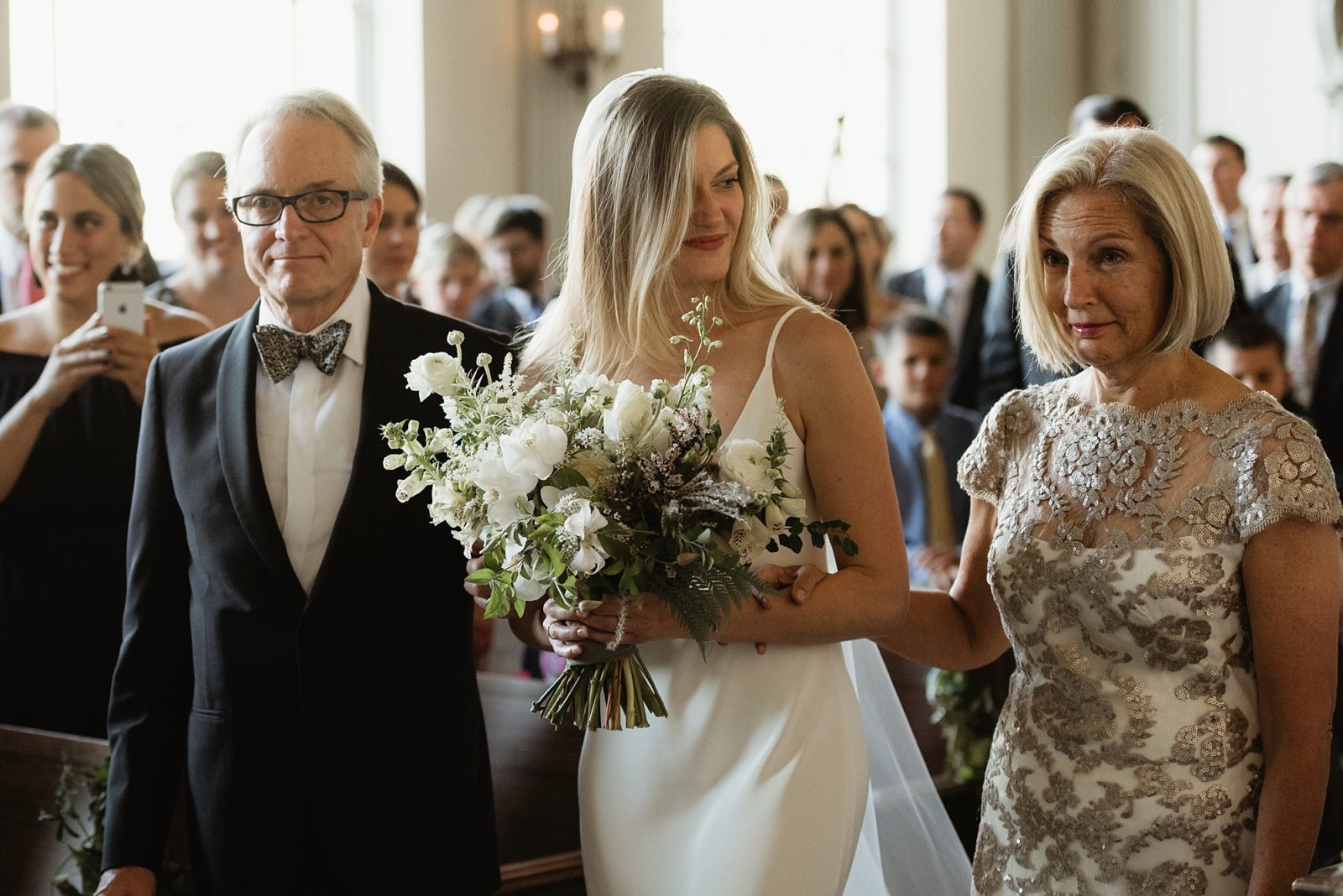 Bride walking down the aisle with parents in modern cream and white wedding
