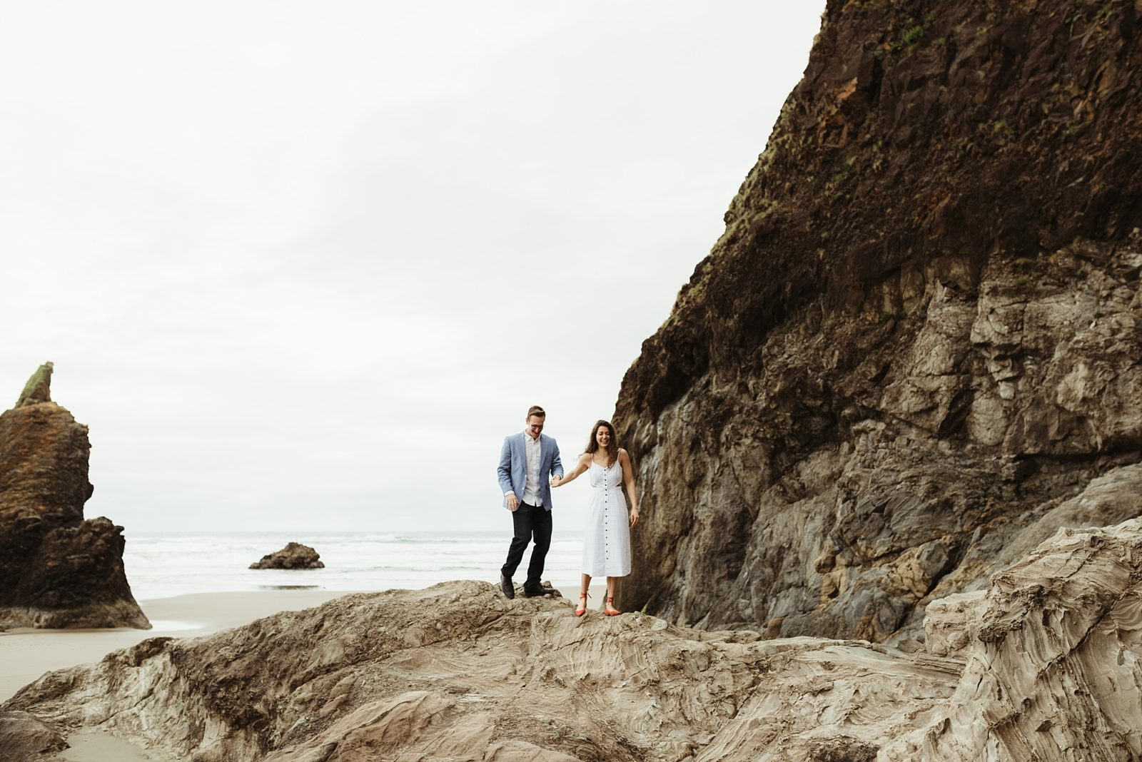 Stylish couple playing on rock at Hug Point on the Oregon Coast during engagement session